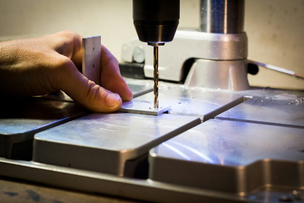 Person drilling a metal bar with a drilling machine, representing setting up tapping equipment