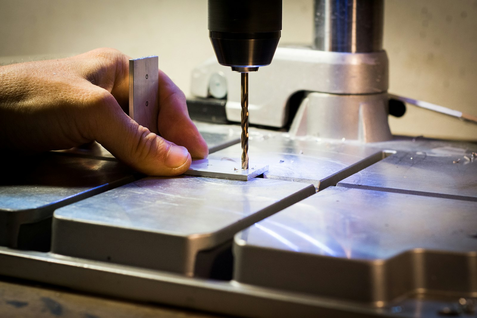 Person drilling a metal bar with a drilling machine, representing setting up tapping equipment