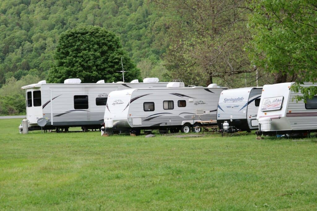 White and brown caravan parked on a green grass field in the daytime, set up for a camping holiday