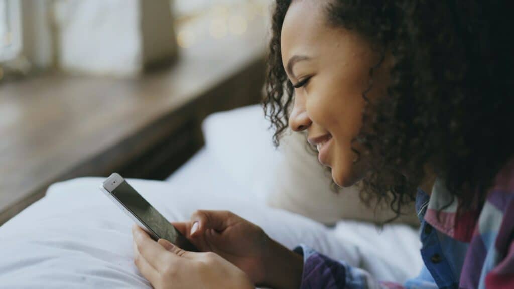 Young woman smiling while using her smartphone in bed, relevant to social media and mental health
