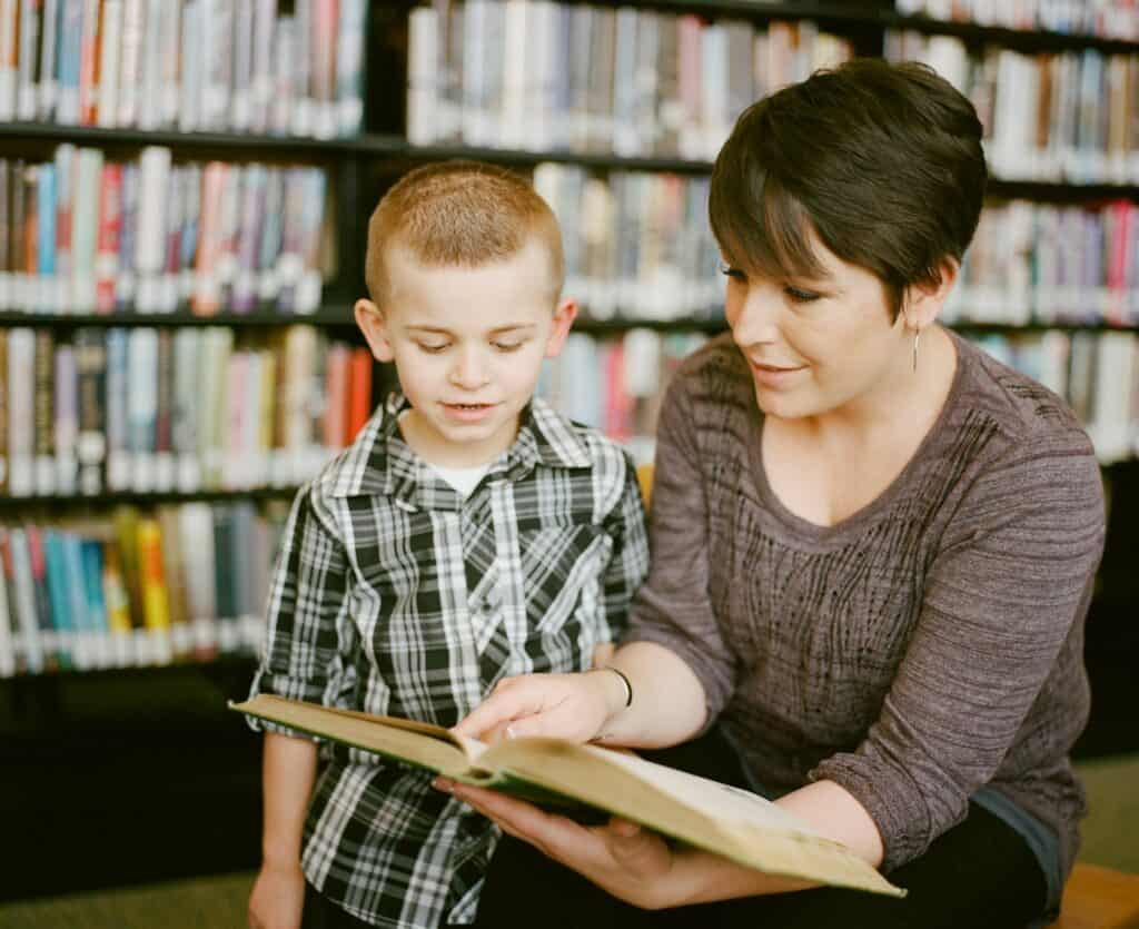 Woman and child reading a book together in a library, reflecting calm, supportive care for a foster child