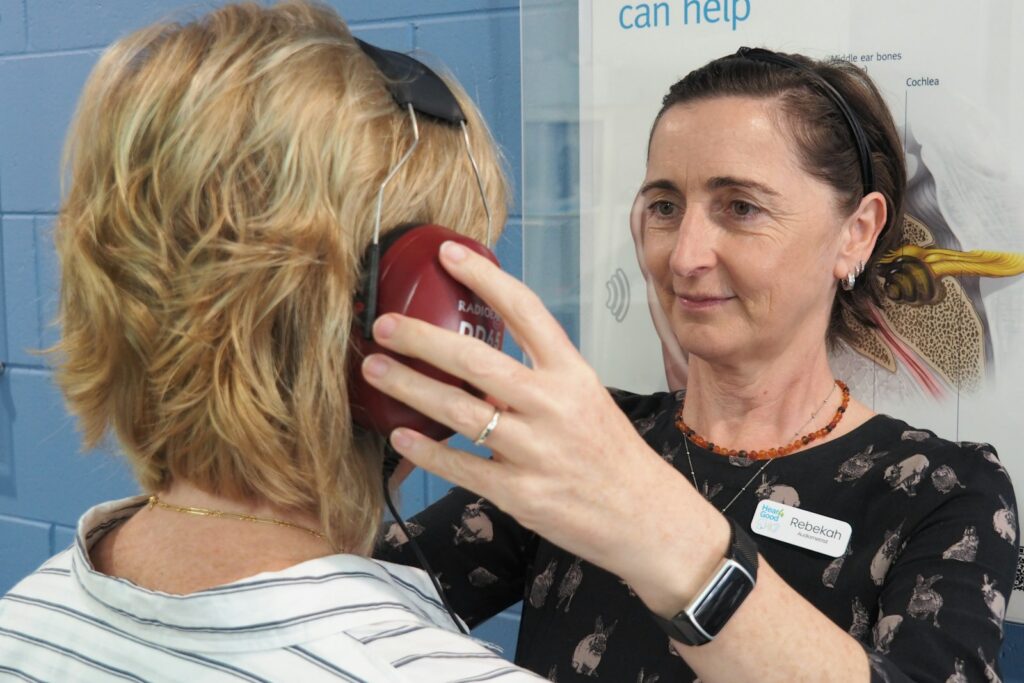 Audiometrist placing headphones on a woman before a hearing test, relevant to when to repeat testing
