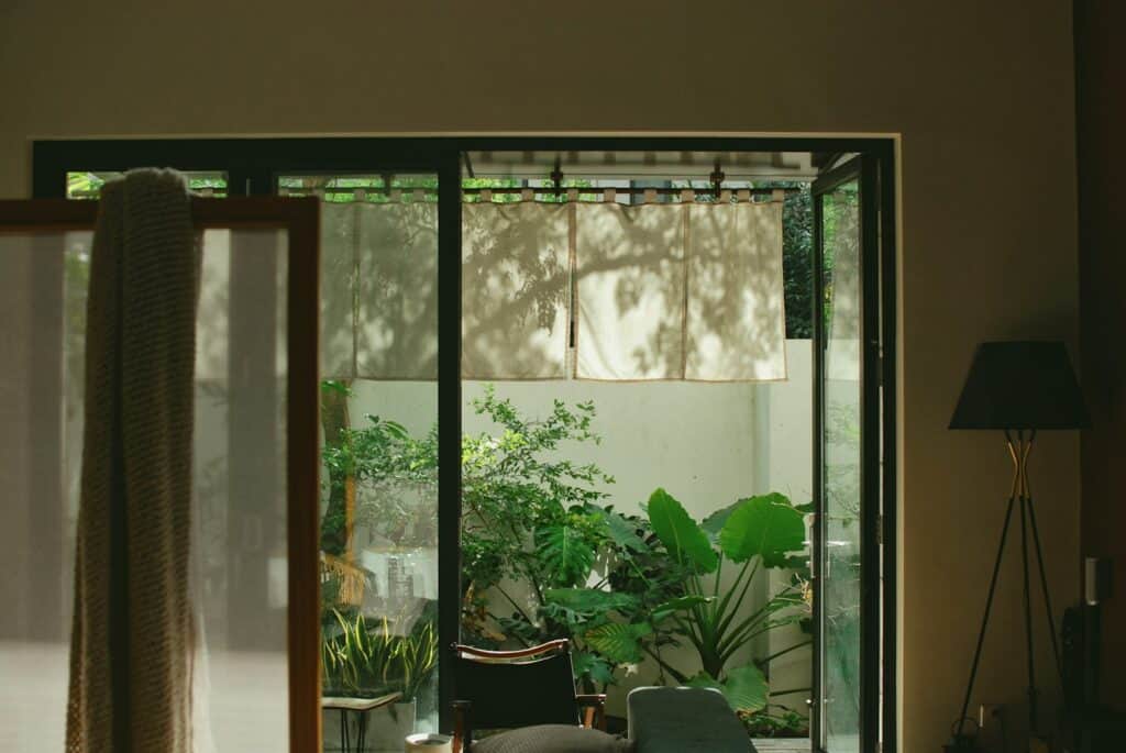 Open glass doors reveal a lush green courtyard garden, showing the indoor-outdoor feel bifold doors can give
