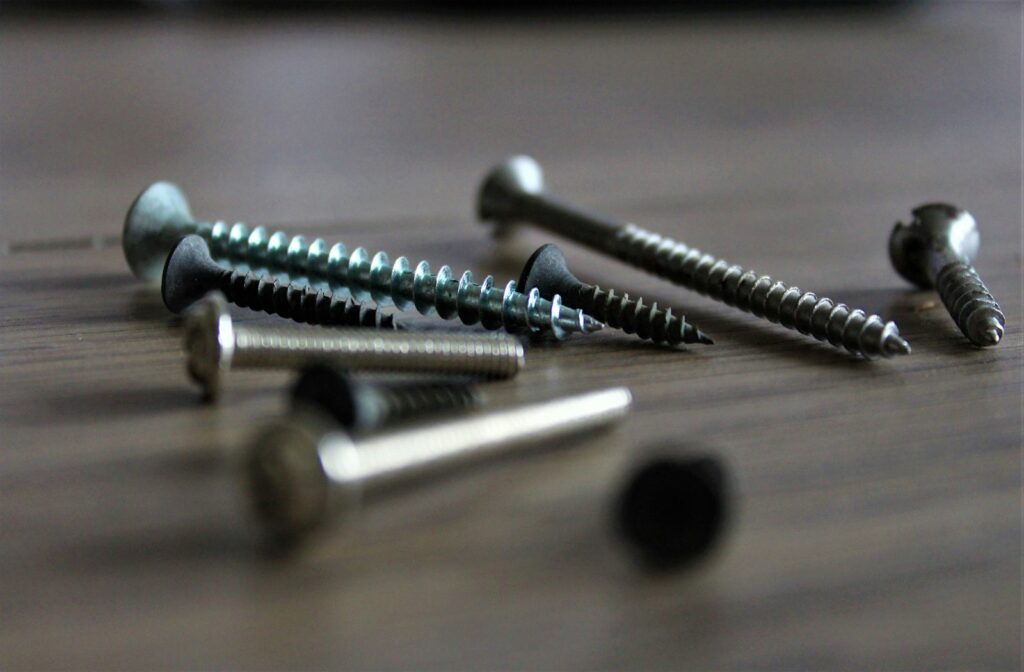 Silver screws and bolts scattered on white background, representing zinc nickel plated fasteners and coating thickness